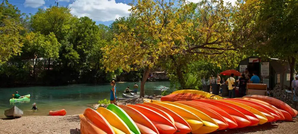 Photo of a stack of colorful kayaks lined up alongside a river in Austin, Tx.