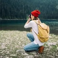 Photo of a woman kneeling on rocky ground while taking a photograph.