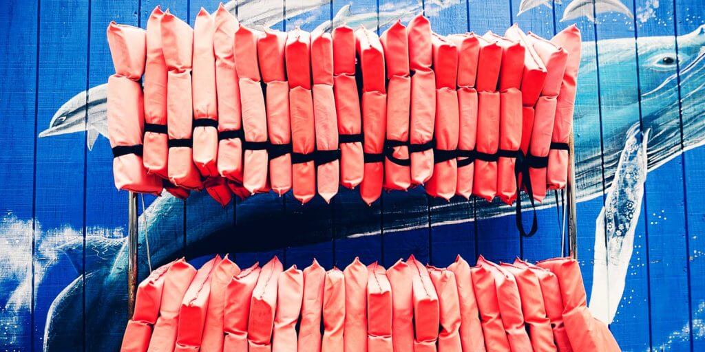 Closeup of 2 racks of orange life jackets against a blue mural with whales on it.