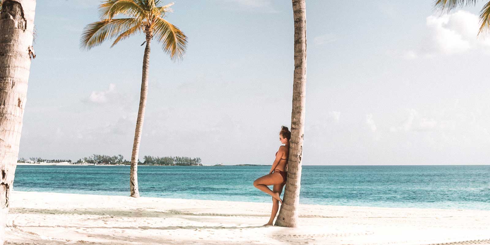 Woman leaning against a palm tree on a deserted beach in Sri Lanka