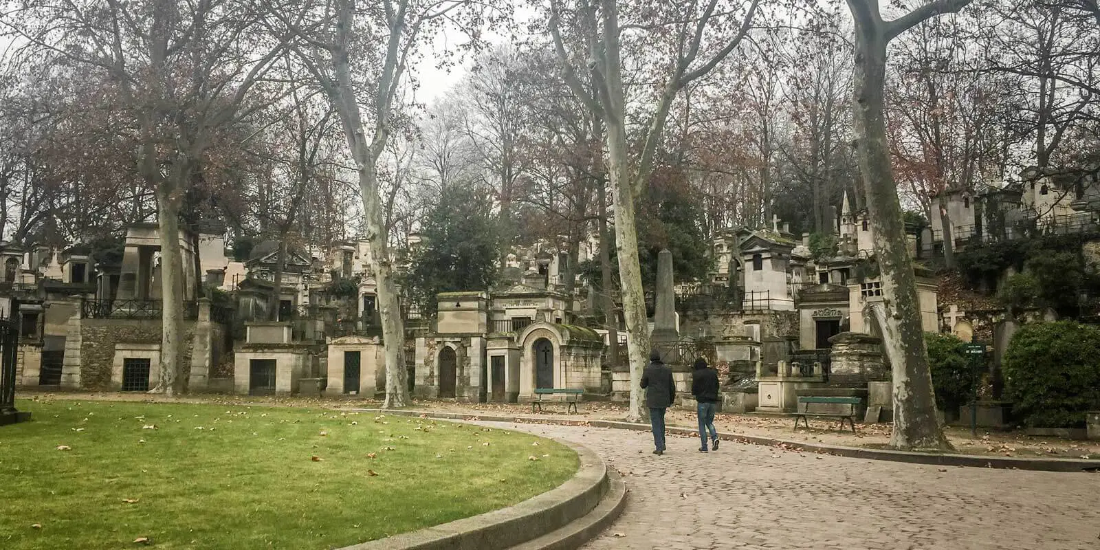 Two people walking through the hauntingly beautiful Père Lachaise cemetery in Paris on a gloomy day.