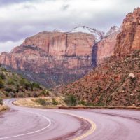 Winding road leading into Zion National Park with mountains and rock formations in the background.