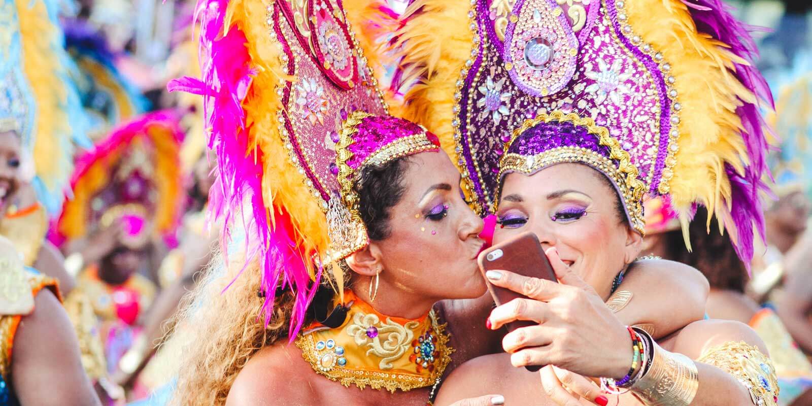 Two women in elaborate Carnival costumes and head dress taking a selfie with a phone.