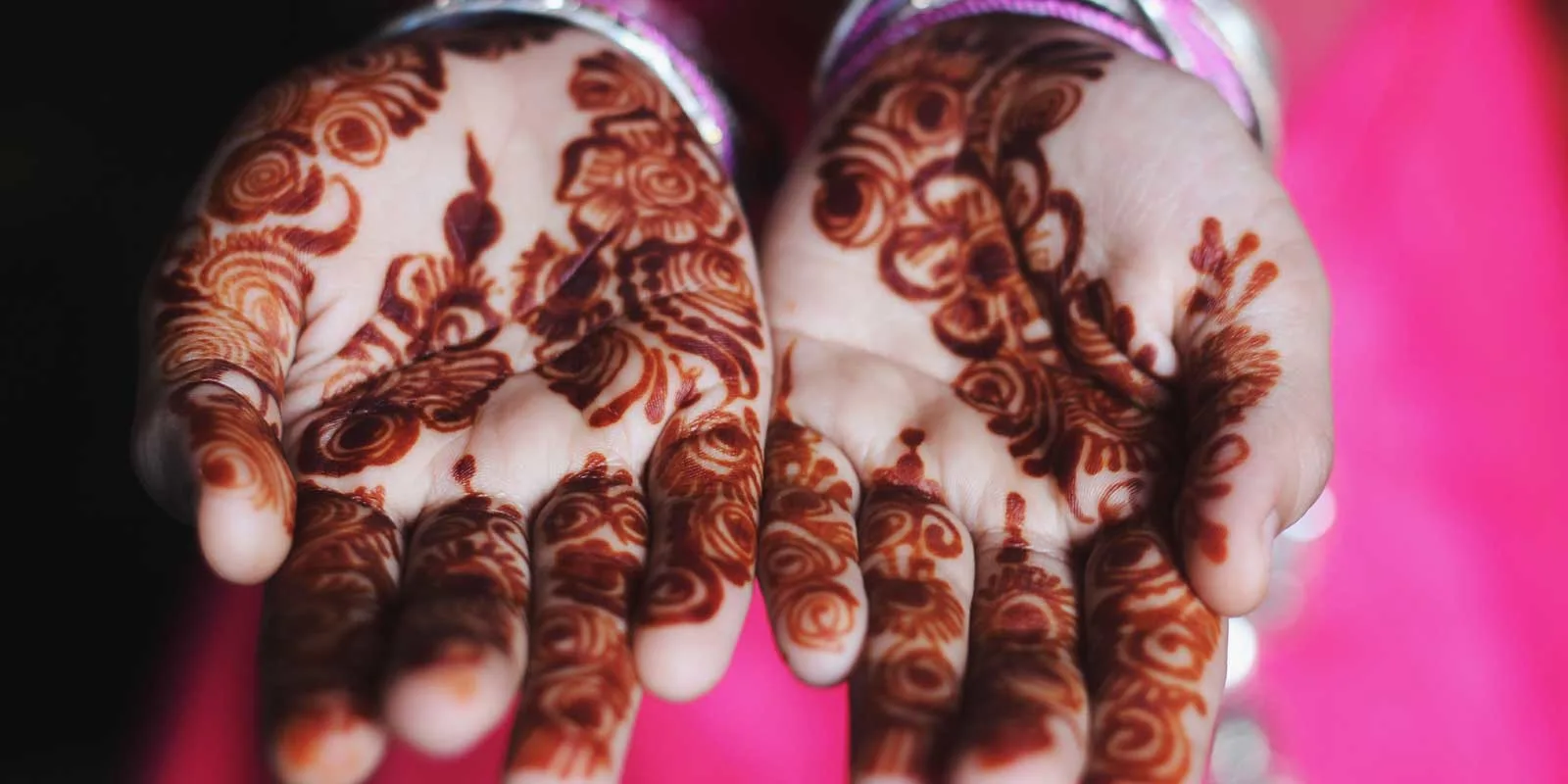 Closeup photo of a woman's hands with intricate henna tattoo on her palms.