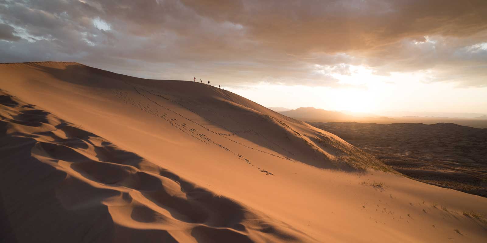Landscape of the Mojave Desert with tiny silhouettes of people climbing the sand
