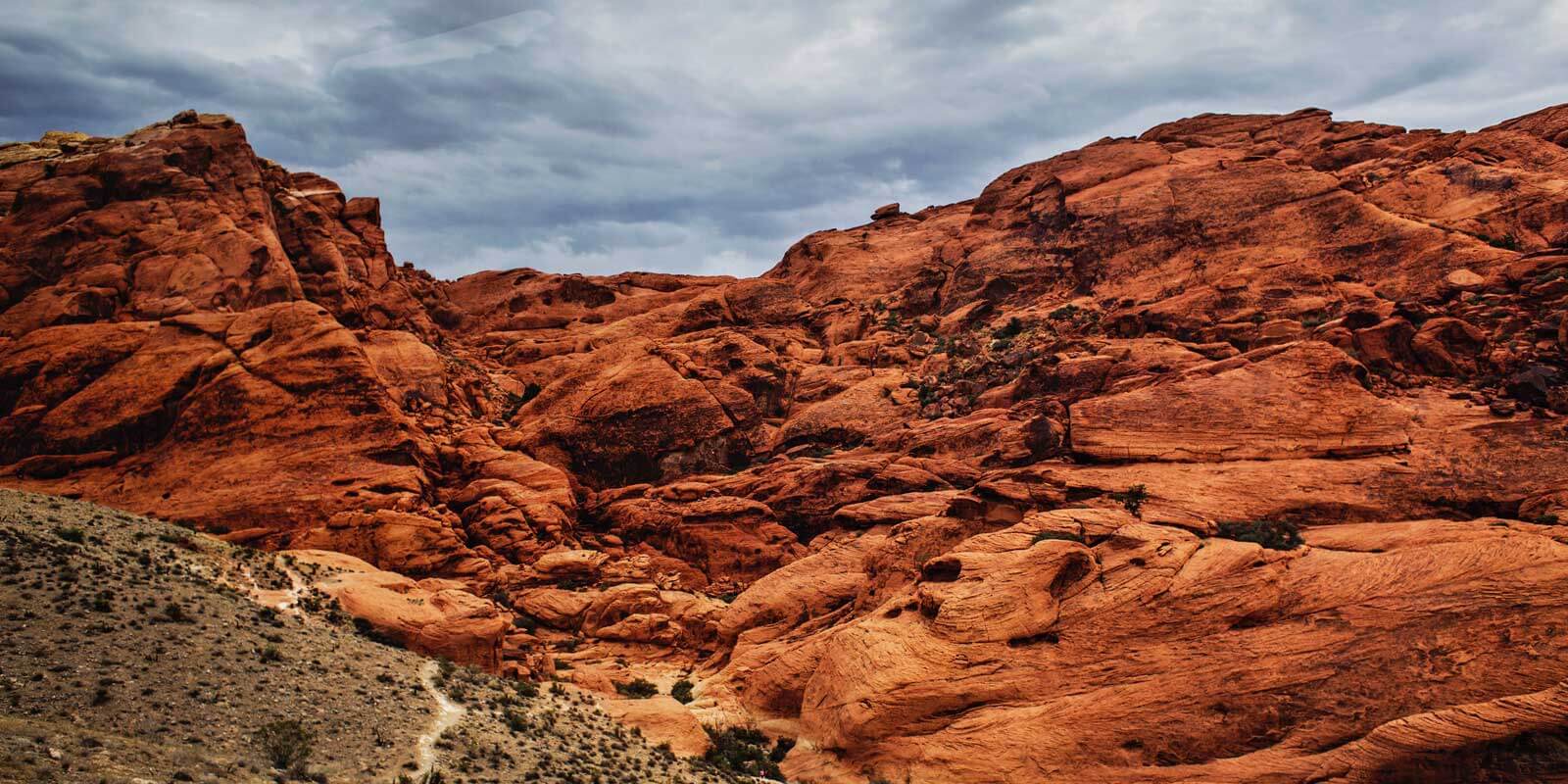 Landscape photo of rusty red rock formations set against a cloudy sky.