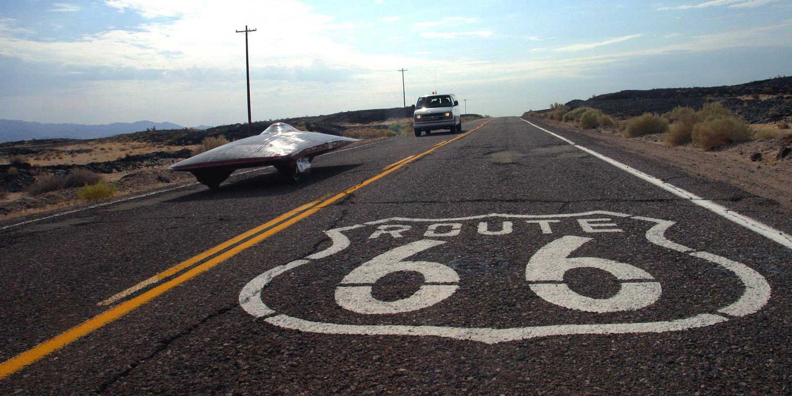 An oddly shaped solar vehicle drives down Route 66, which is painted on the pavement.