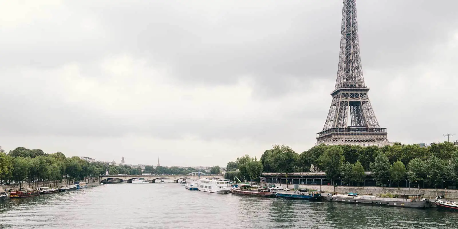 Landscape photo of the Seine River with the Eiffel Tower in the background on a gray, stormy day.