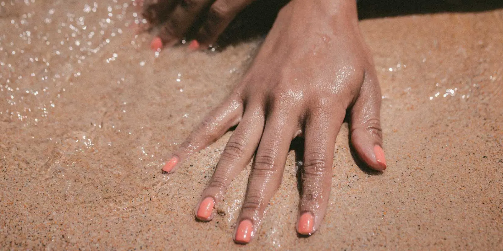 Close up of a women's freshly manicured hands set against a sandy beach.