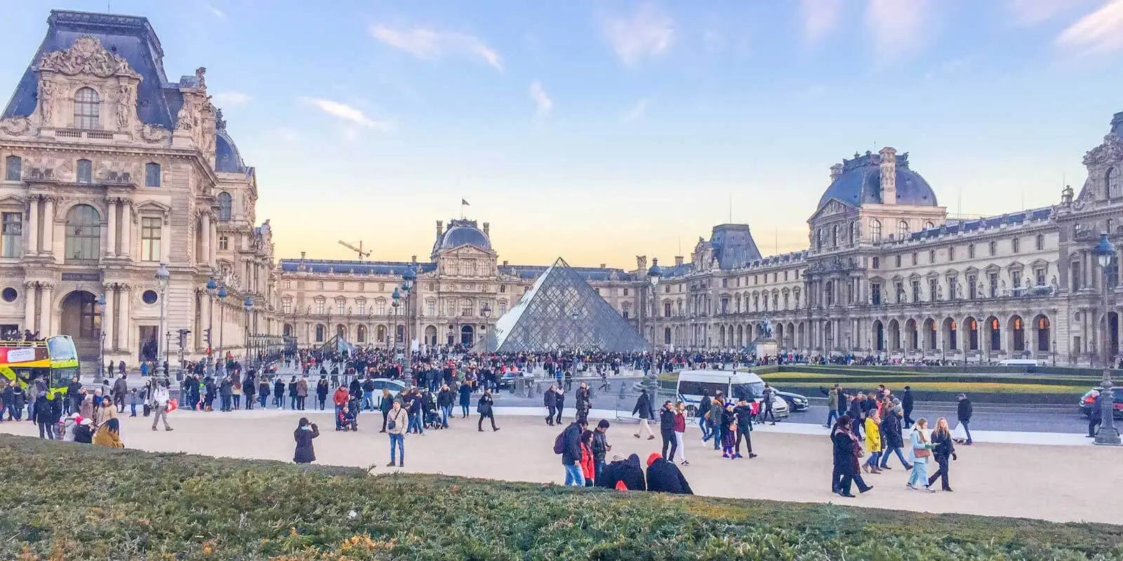 Crowds walking outside the front entrance to The Louvre at sunset.