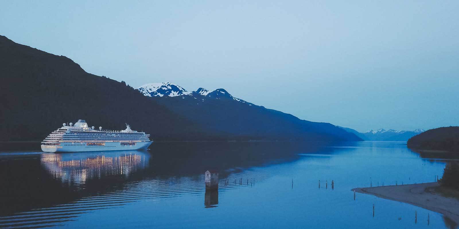 Landscape view of a cruise ship in Alaska, with snow capped mountains in the background.