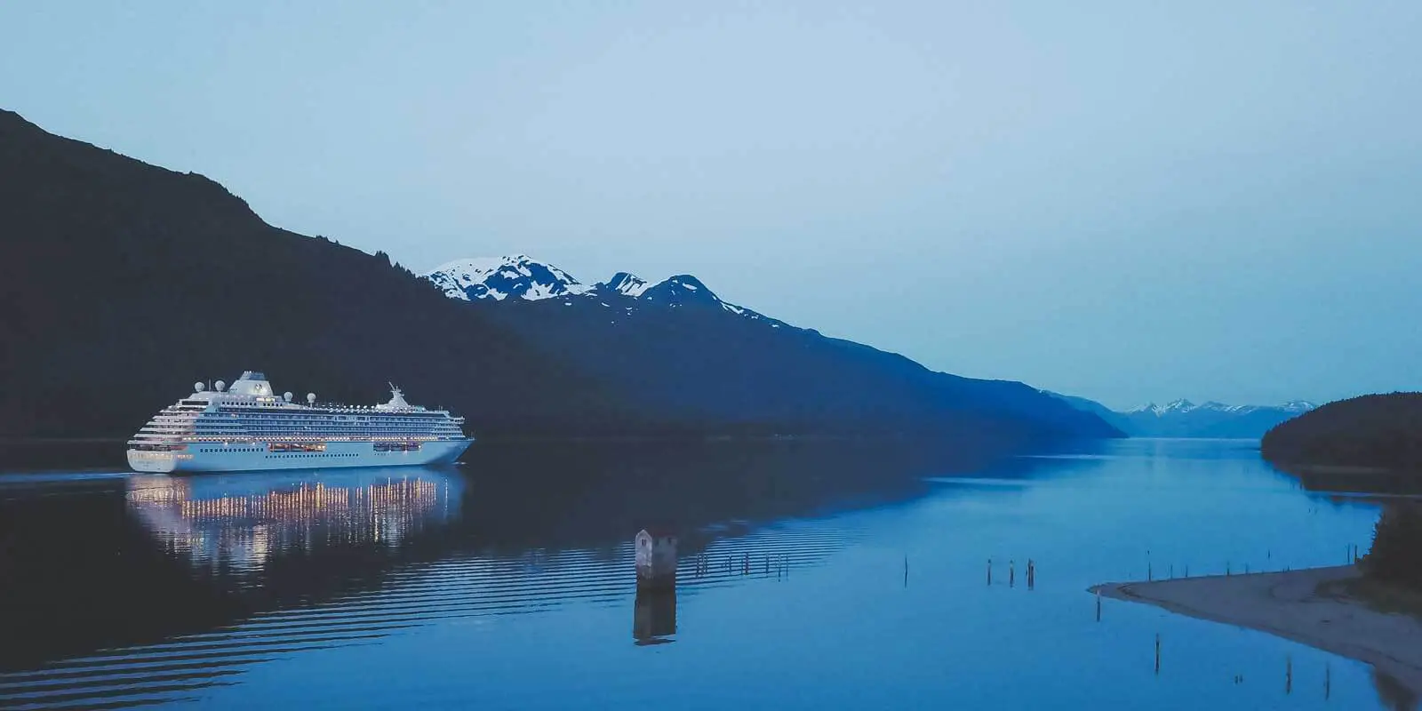 Landscape view of a cruise ship in Alaska, with snow capped mountains in the background.
