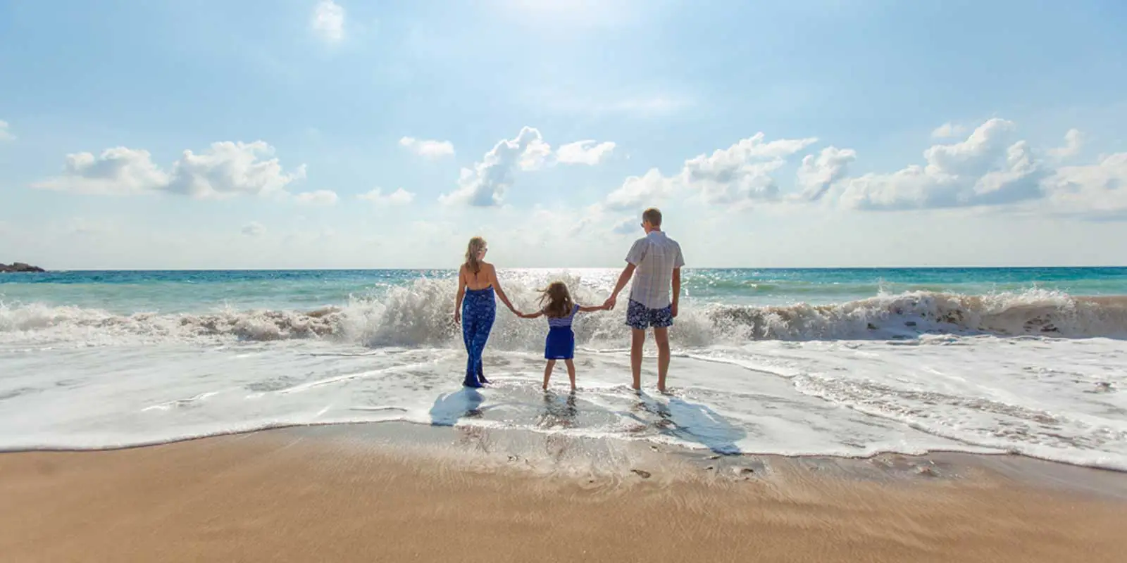 Photo of a mom, daughter, and dad holding hands at the beach.