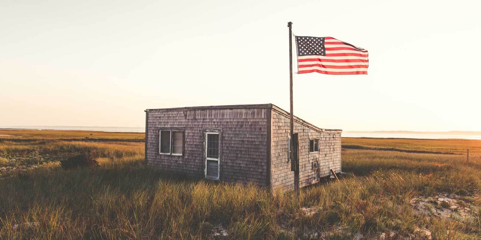 American flag waves in the air next to a seaside shack in Cape Cod