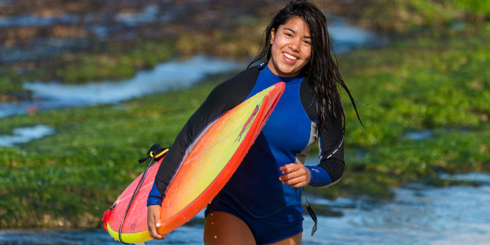 Woman wearing a rashguard and carrying a surfboard on a beach