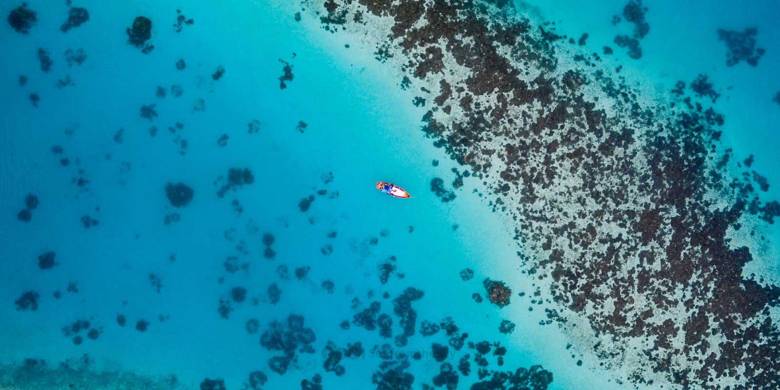 Aerial shot of coral reef near the Maldives, with an orange boat.