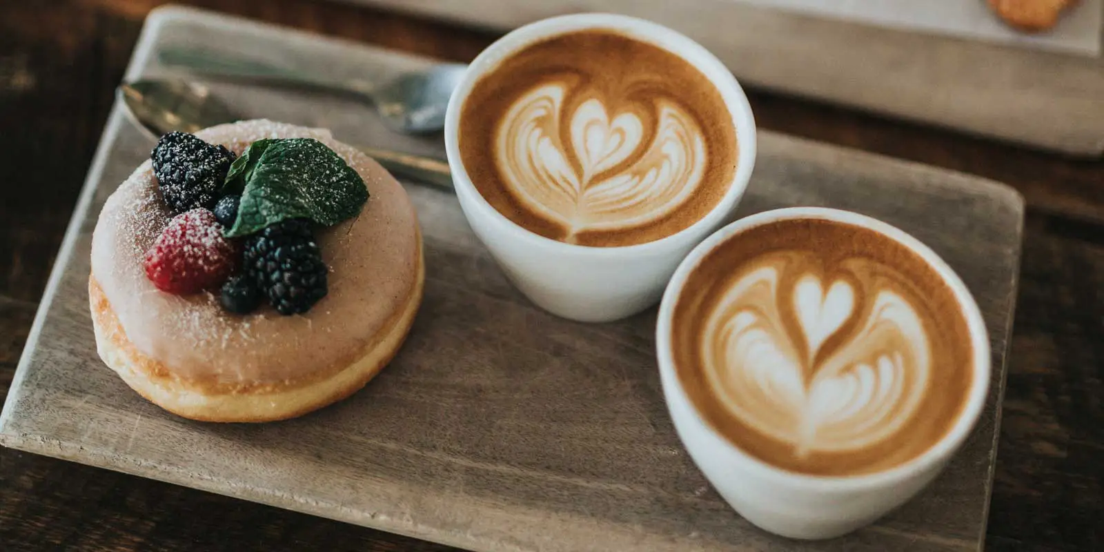 Flatlay photo of 2 cappucinos and a donut with berries on top.