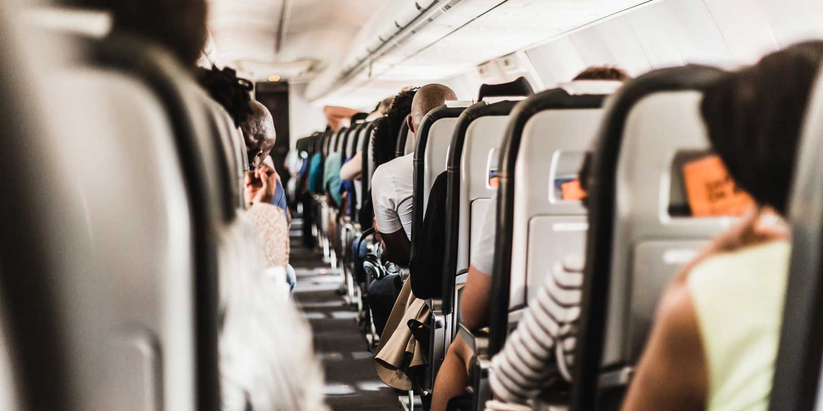 View of plane seats filled with people from back of plane.