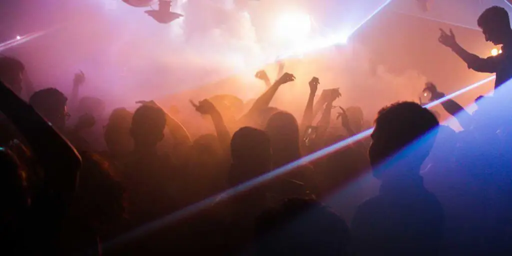 Photo inside a nightclub with silhouettes of dancing people and flashing lights.