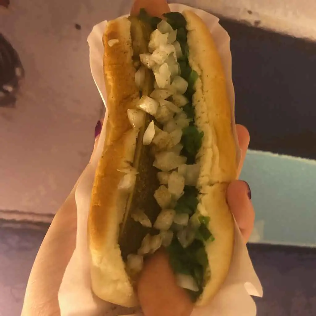 Close up of a steamed hot dog covered in onions, relish, and a pickle from Haute Doggery in Las Vegas.