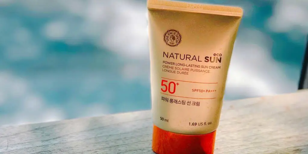 Closeup of a tube of sunscreen sitting next to a pool.