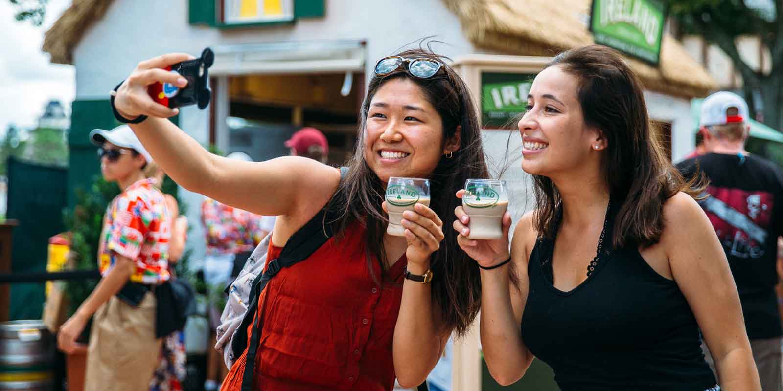 2 women pose for a selfie with a drink from the Ireland food stall at Epcot's International Food & Wine Festival.