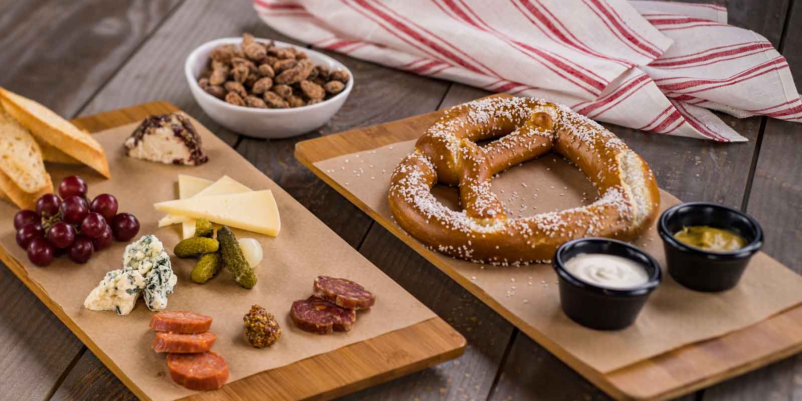 Flat lay photo of the food available at the BaseLine Tap House at Disney World's Hollywood Studios. In the photo are a giant baked pretzel and dips, a charcuterie board, and bar nuts.