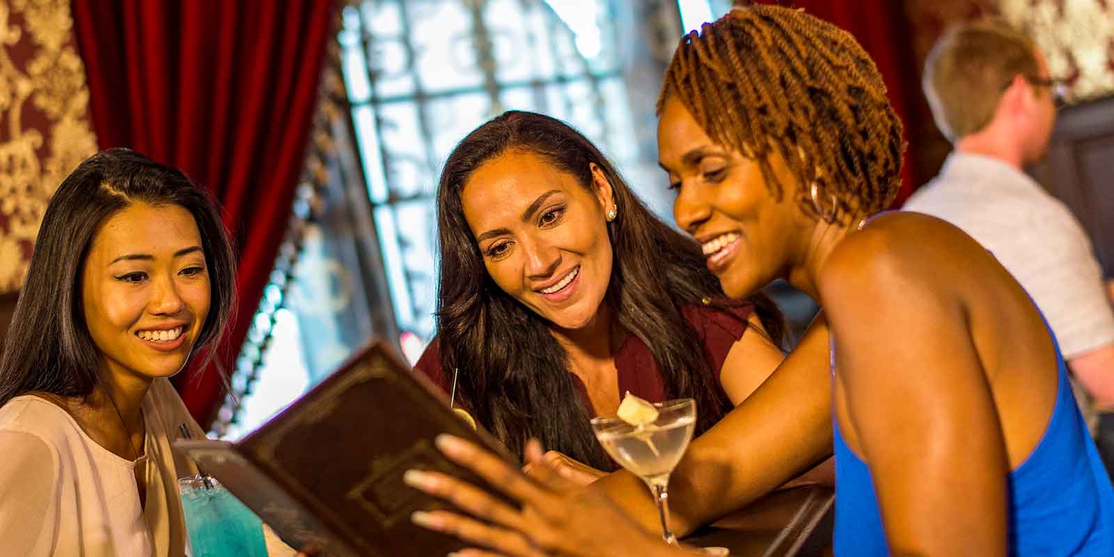 Three women peruse a drink menu at Disney Boardwalk's AbracadaBar.
