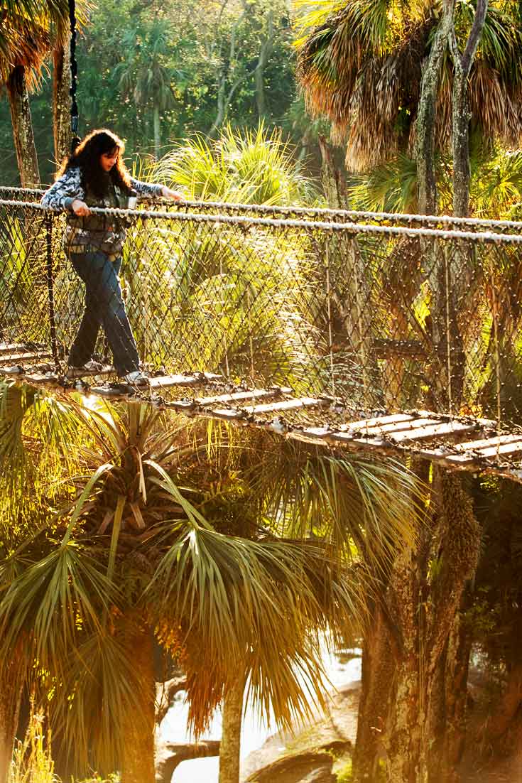 A woman walks across a rope and plank bridge at Disney's Animal Kingdom park.