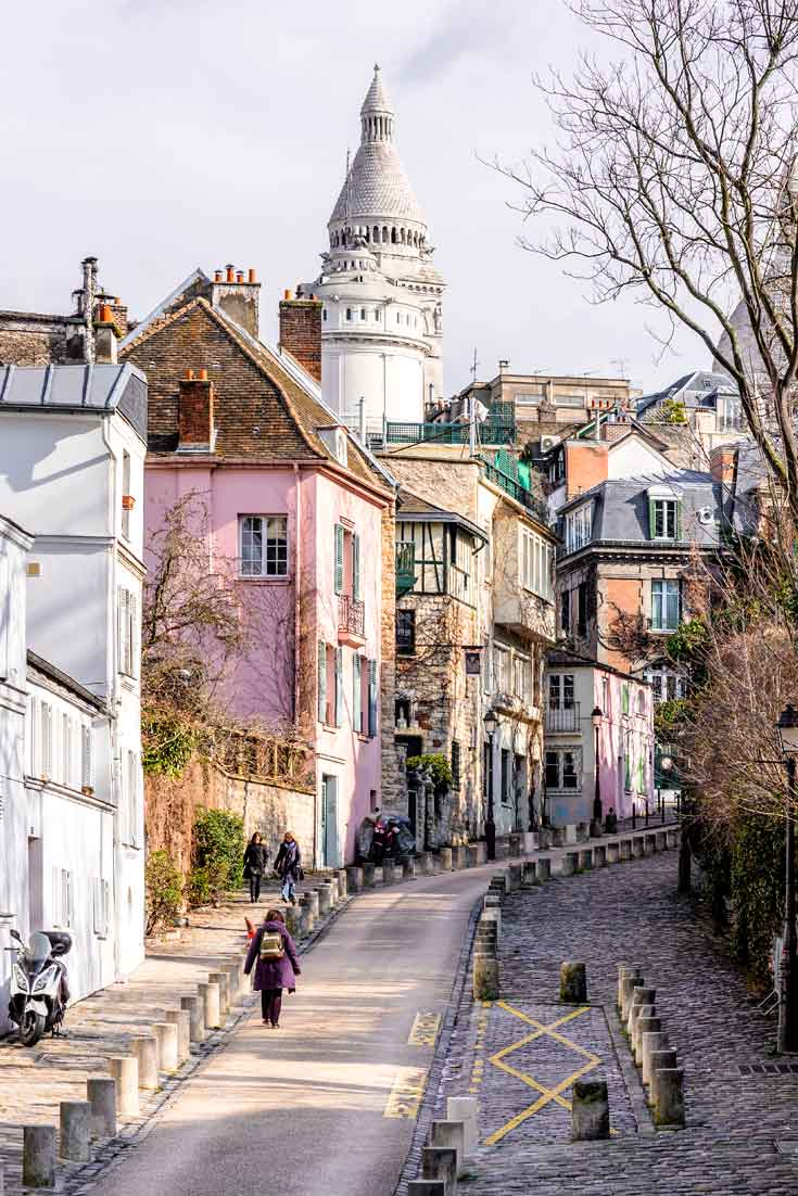 Portrait shot of a hilly street in Montmartre, Paris, France with colorful buildings, such as white, pink, and yellow.