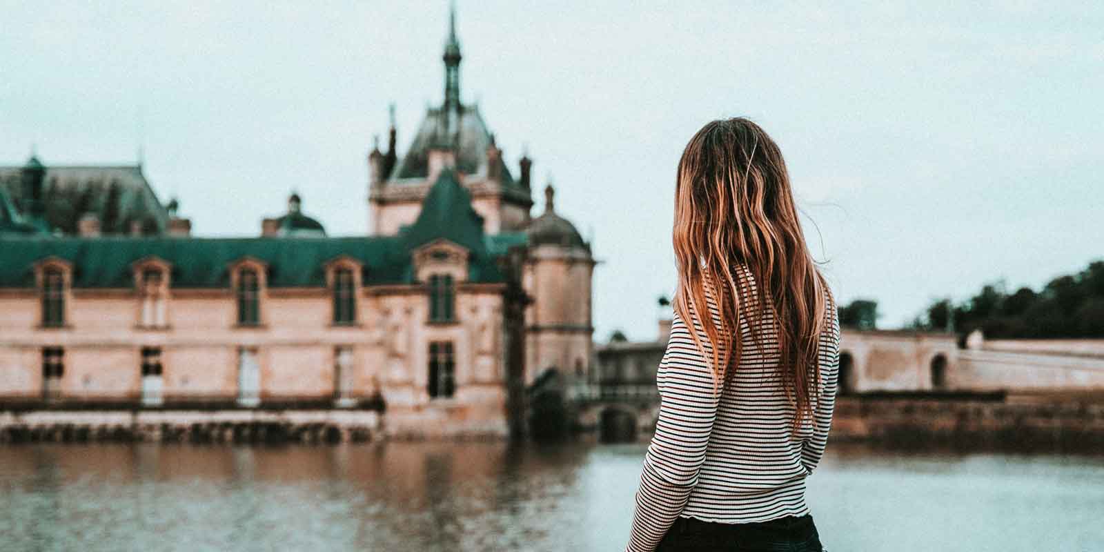 Landscape view of a woman looking at the Château de Chantilly in the background.