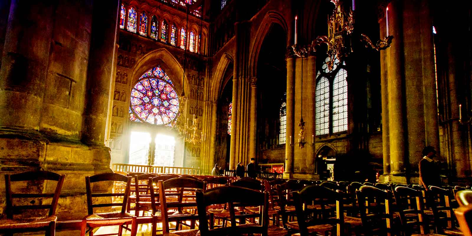 Landscape view inside the Notre Dame de Reims church, including the sun shining through a stained glass window.