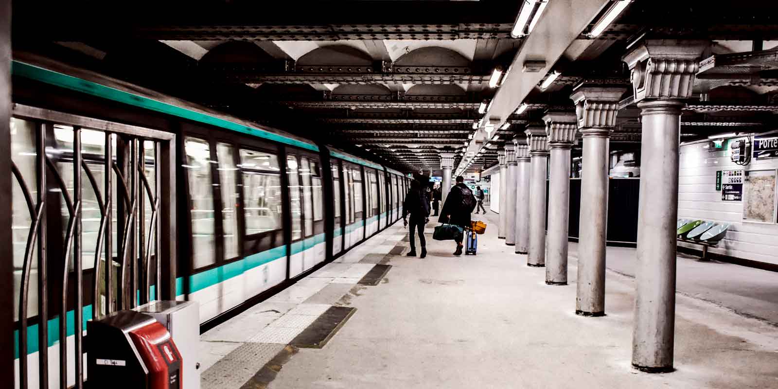 A Paris Metro train pulls into a train station while a few people wait to board.