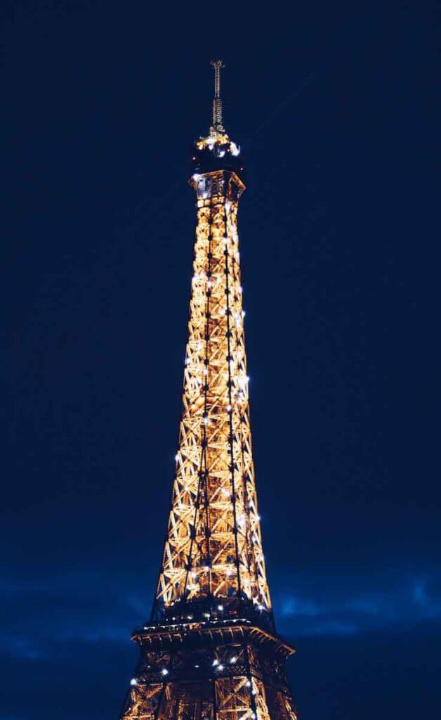 Close up photograph of the top of the Eiffel Tower in Paris, France light up at night.