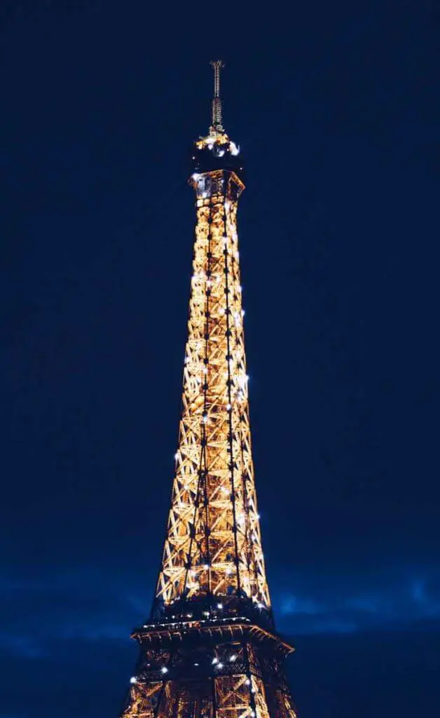 Close up photograph of the top of the Eiffel Tower in Paris, France light up at night.