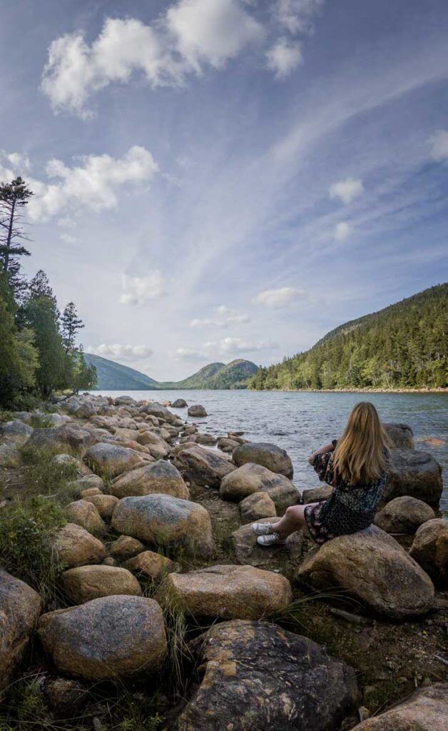 Woman sitting on a rocky lake shore overlooking Jordan Pond at Acadia National Park