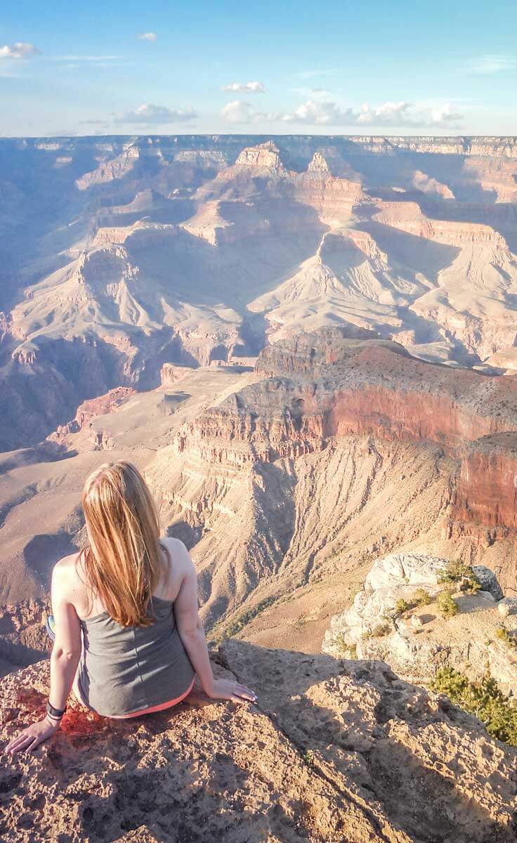 Woman sits on a ledge overlooking the Grand Canyon in Arizona.