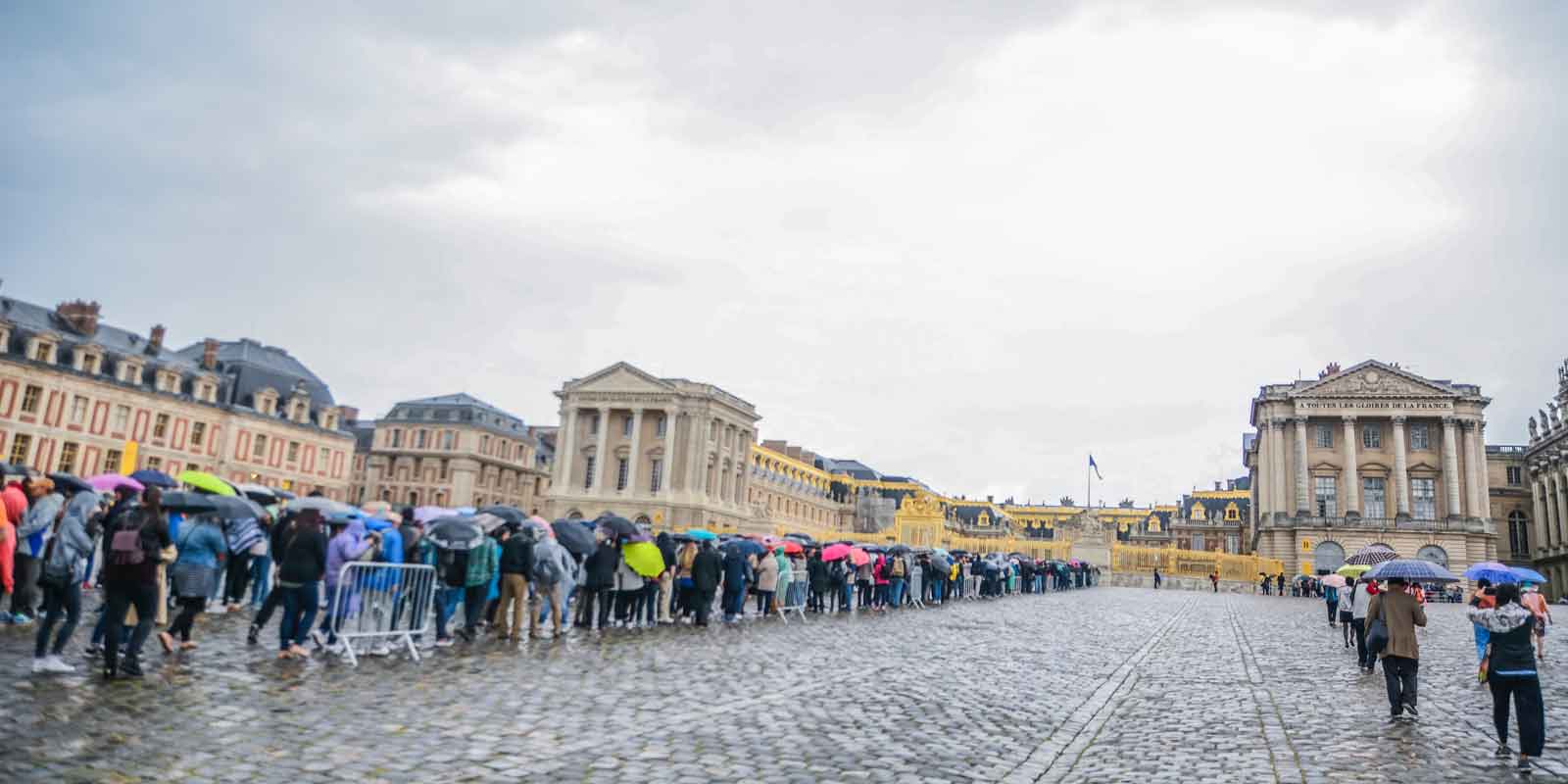 Photograph of a large crowd of people lining up outside the Palace of Versailles in France.
