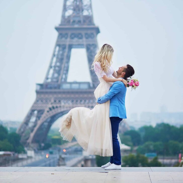 Photo of a man holding a woman up in the air with the Eiffel Tower in the background.
