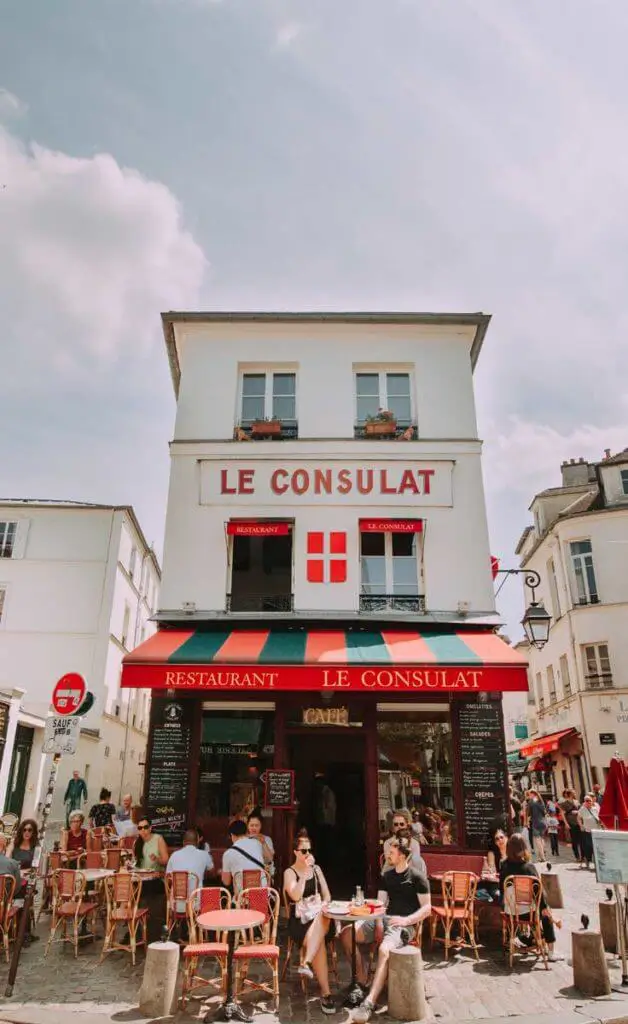 Photograph of Le Consulat restaurant in Paris, France, with people dining outside on a clear day.