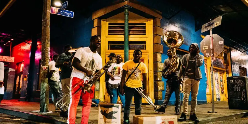 A group of young people perform music with brass instruments on a corner of Frenchman Street in New Orleans, a section well known for Jazz clubs.