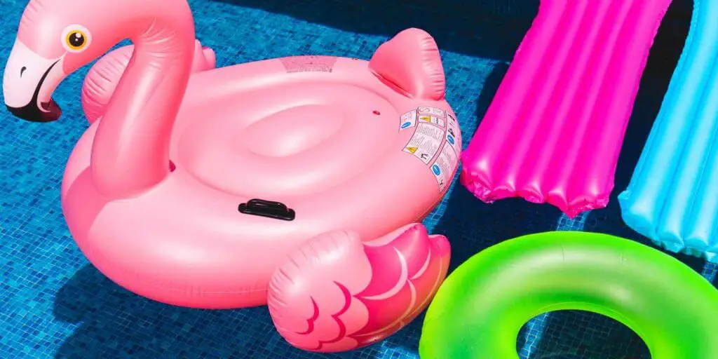 Close up of a bunch of pool floats in a pool, including a pink flamingo, a bright pink floating lounger, a turquoise floating lounger, and a neon green tube.