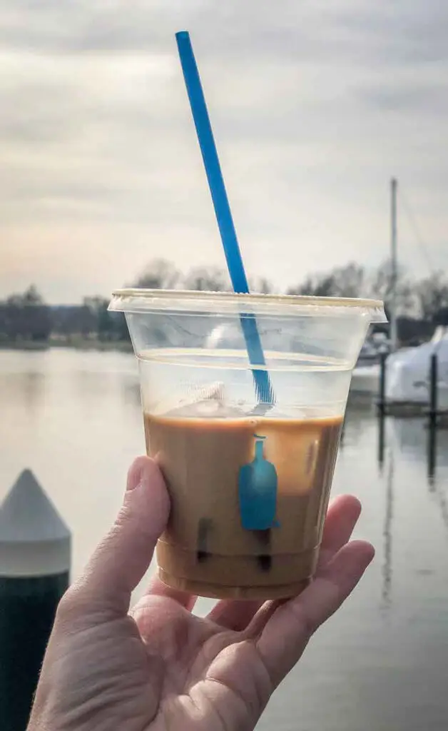 Closeup of a half empty New Orleans style iced coffee from Blue Bottle Coffee in front of a marina in DC.