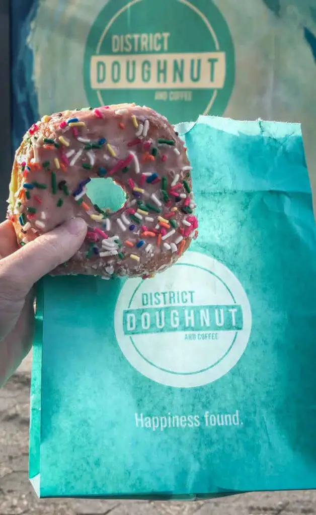 Closeup of a sprinkle-covered doughnut with a teal blue bag from District Doughnut in DC.