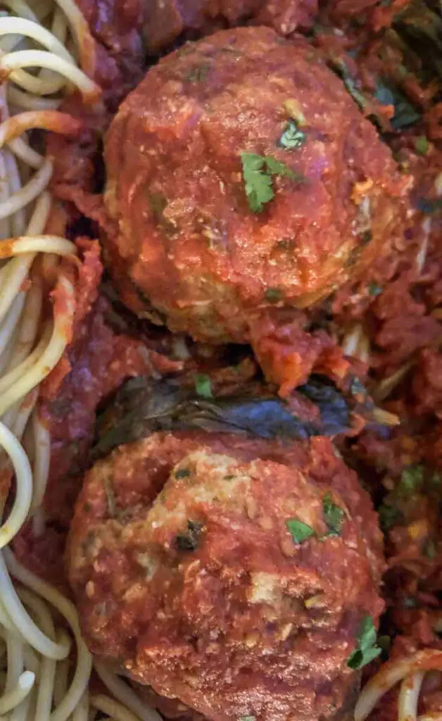 Closeup of 2 large meatballs in a plate of red sauce and spaghetti noodles.