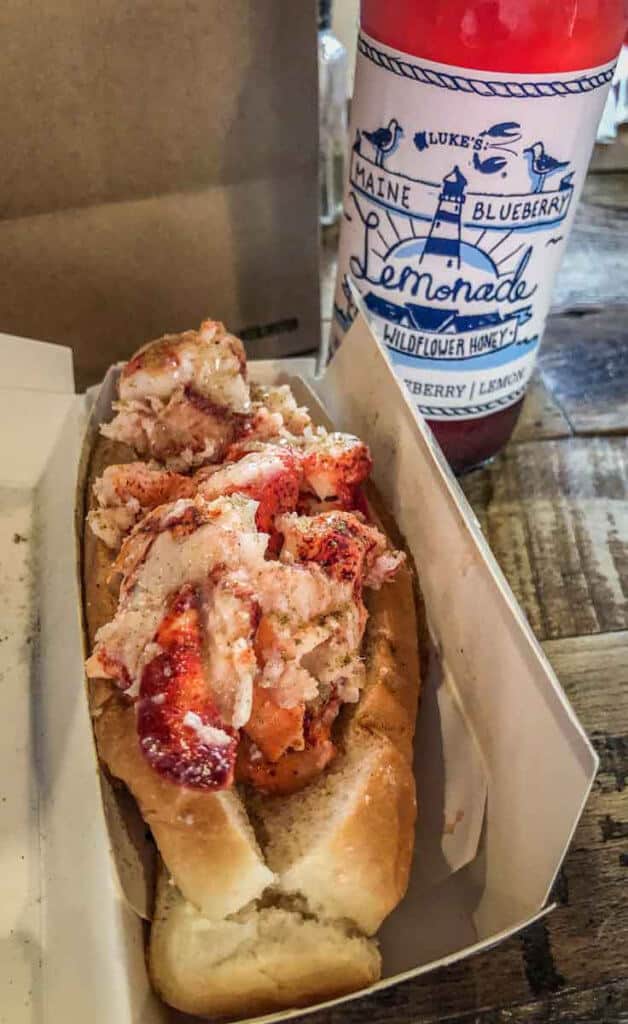 Closeup of lobster salad in a hot dog bun with a bottle of blueberry lemonade in the background.