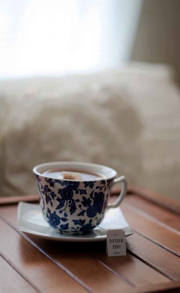 Close up of a cup of tea in a blue floral print tea cup with a tea tag that says "Drink Me."