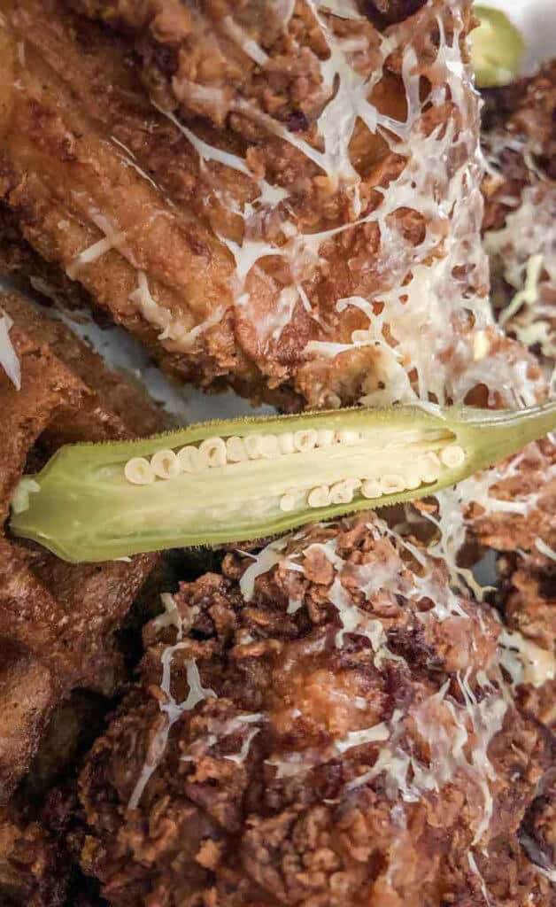 Closeup shot of fried chicken covered in shredded cheese and okra, on top of waffles.