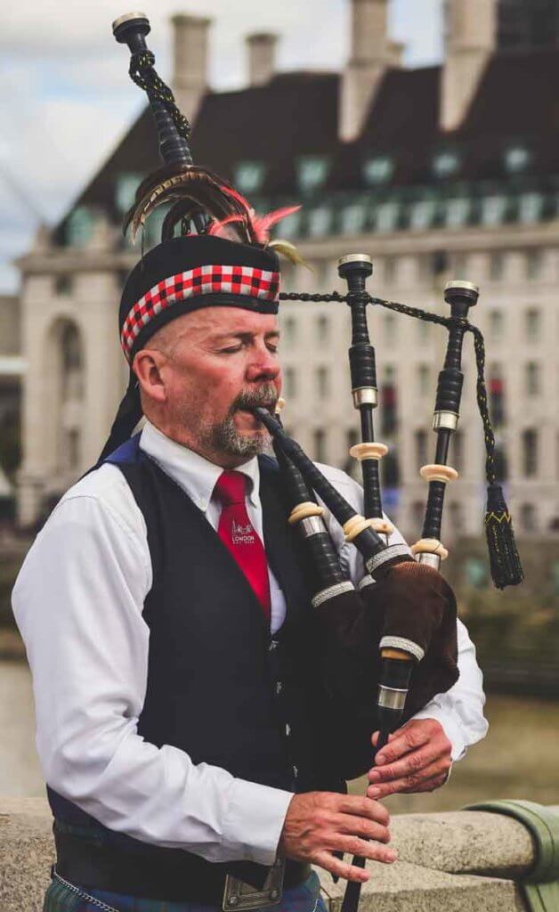 Closeup of a man wearing a kilt uniform, playing bagpipes.