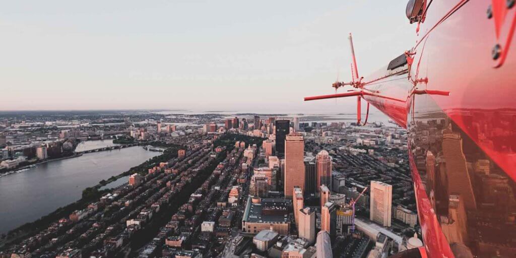 Aerial view of Boston and the Charles River with the tail view of a red helicopter in the corner.
